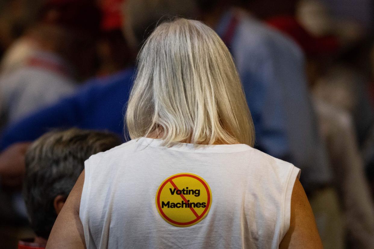 An attendee wears a sticker calling for the end of voting machine use at the Georgia Republican Party's 2023 State Convention in Columbus, Georgia. Her back is to the camera, and the sticker is on the back of her shirt—it says "voting machines" with a slash-through.