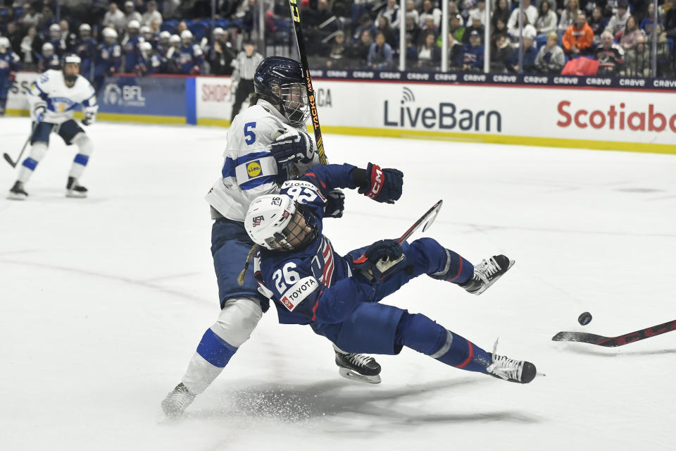 United States forward Kendall Coyne Schofield (26) is tripped by Finland defensewoman Siiri Yrjola (5) during the second period in the semifinals at the IIHF women's world hockey championships in Utica, N.Y., Saturday, April 13, 2024. Yrjola was called for holding on the play. (AP Photo/Adrian Kraus)