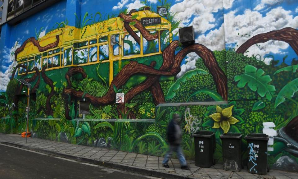 A person wearing a face mask walks past a city of Melbourne inspired street art mural in Melbourne, Australia.