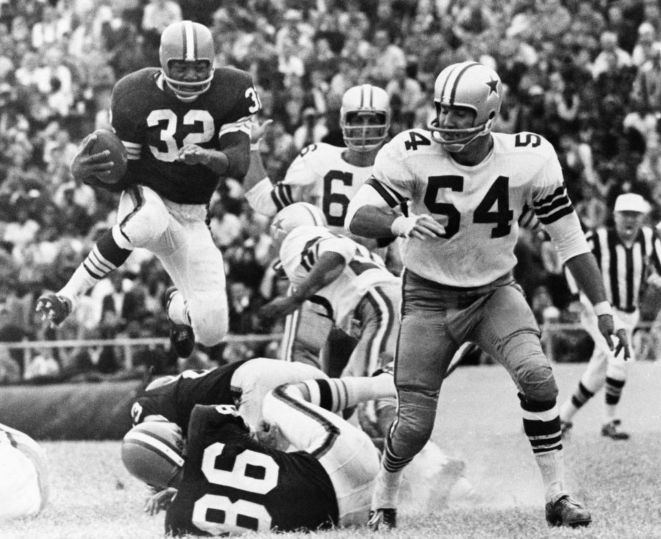 Cleveland Browns fullback Jim Brown leaps for a gain over teammate Gary Collins (86) in the third quarter at the Dallas Cowboys, Oct. 19, 1964. Watching are Cowboy players George Andrie (66) and Chuck Howley (54). The Browns won 20-16.