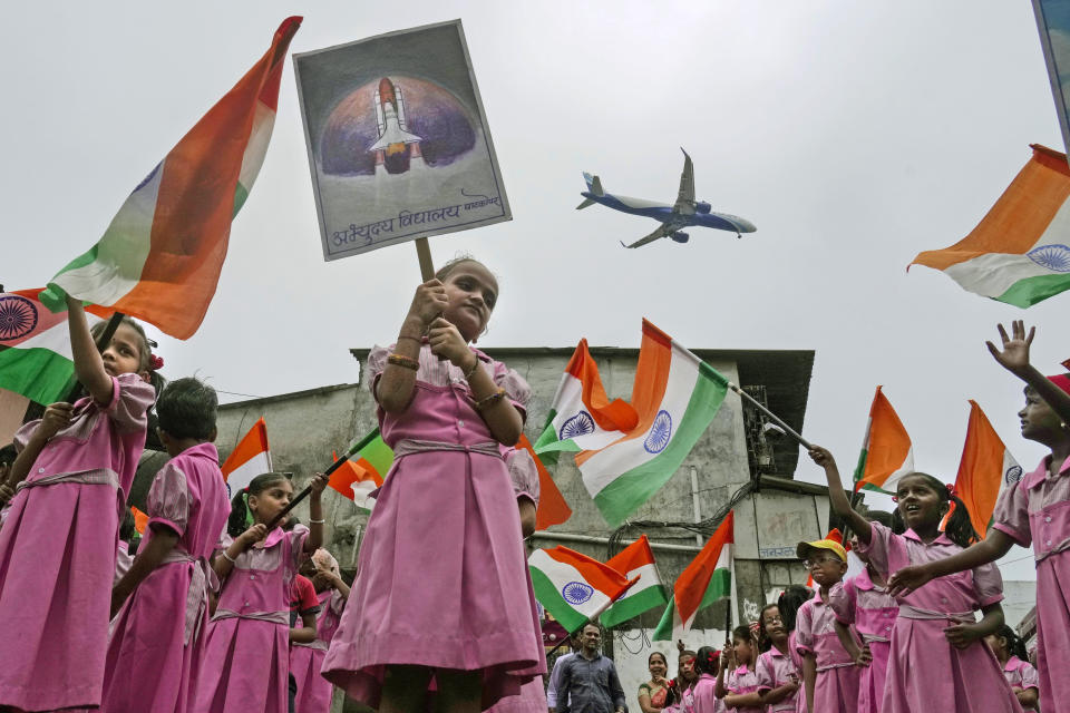 FILE - An aircraft prepares to land as children cheering for the successful landing of India's moon craft Chandrayaan-3, on the moon surface, wave Indian flags at a school near the airport in Mumbai, India, Tuesday, Aug.22, 2023. (AP Photo/ Rajanish Kakade, File)