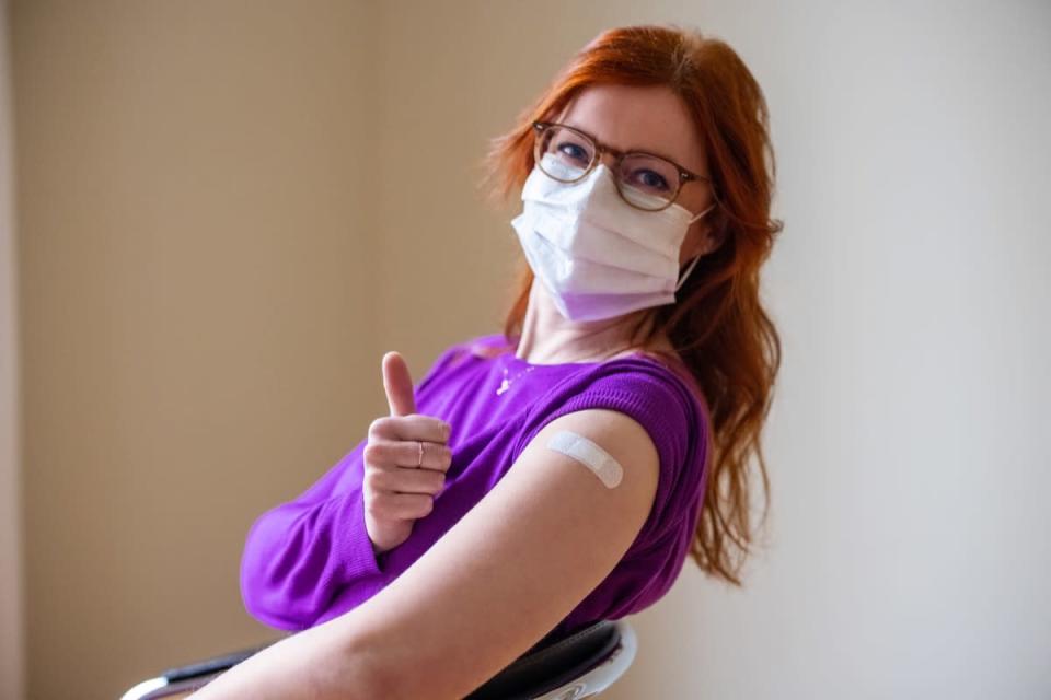 Woman wearing face mask looking at camera showing thumbs up after getting the covid-19 vaccine.