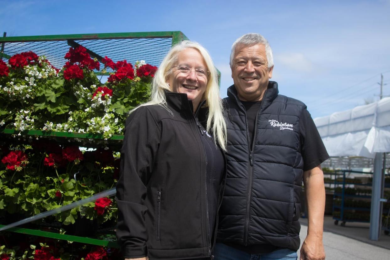 Parkdale Market vendors Brigitte and Michel Robinson pose for a photo next to some of their flowers as they pause from preparing their stall for the 2024 season. This year will mark the 100th anniversary of the market west of Ottawa's downtown. (Trevor Pritchard/CBC - image credit)