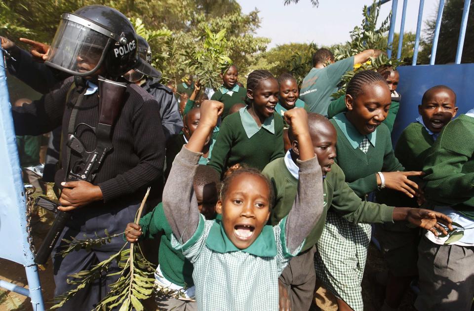 Students from Langata primary school run past riot police as they protest against a perimeter wall illegally erected by a private developer around their school playground in Nairobi