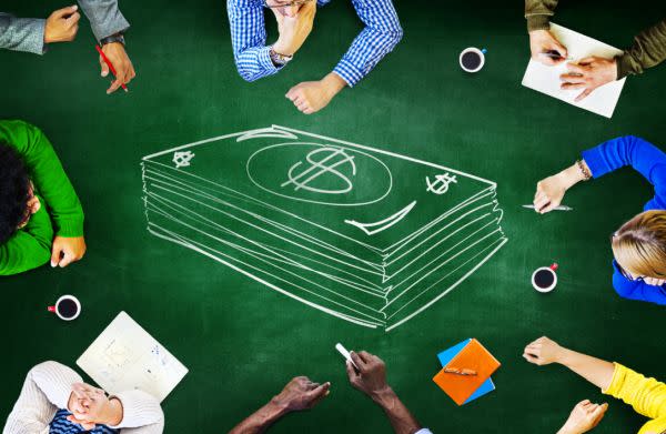 students sit at a green table surrounding a chalk drawing of a stack of cash