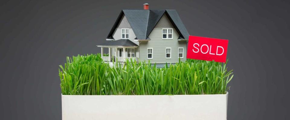 Close up of house model with green grass and sold tablet on grey background. Concept of real estate and sales