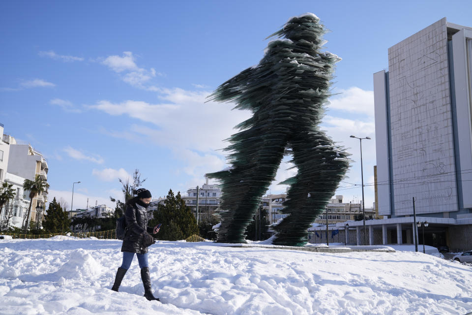 A woman walks past a the Runner, sculptured by Kostas Varotsos, after a snowstorm, in Athens, on Tuesday, Jan. 25, 2022. A snowstorm of rare severity disrupted road and air traffic Monday in the Greek capital of Athens and neighboring Turkey's largest city of Istanbul, while most of Greece, including — unusually — several Aegean islands, and much of Turkey were blanketed by snow. (AP Photo/Thanassis Stavrakis)