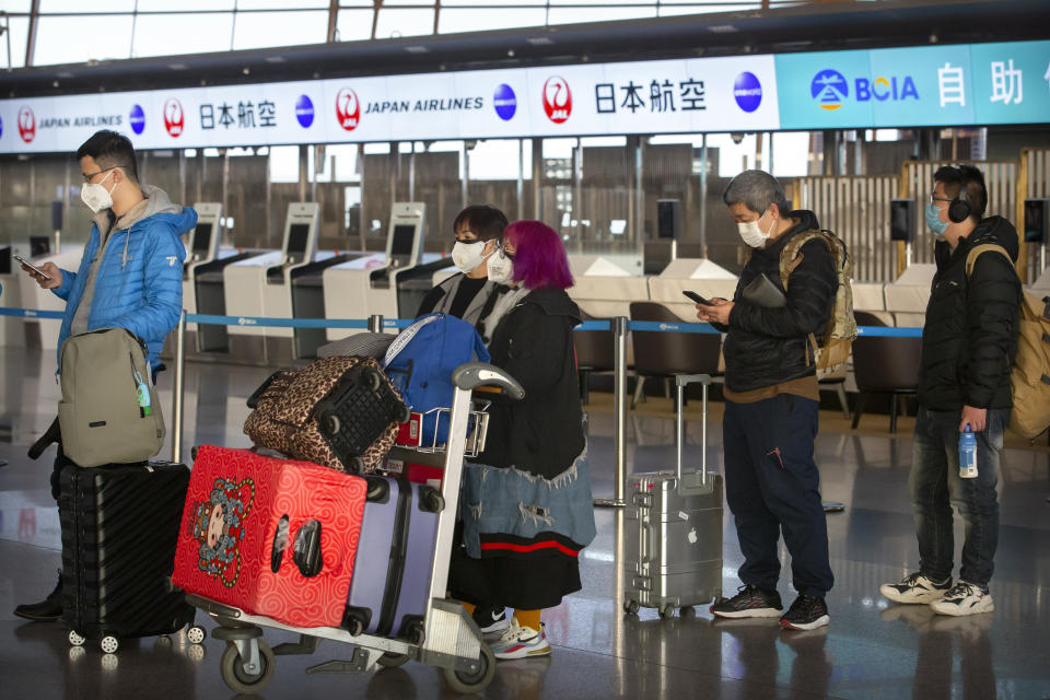 Travelers wearing face masks line up near the Japan Airlines check-in counters at Beijing Capital International Airport in Beijing, Thursday, Jan. 30, 2020. China counted 170 deaths from a new virus Thursday and more countries reported infections, including some spread locally, as foreign evacuees from China's worst-hit region returned home to medical observation and even isolation. (AP Photo/Mark Schiefelbein)