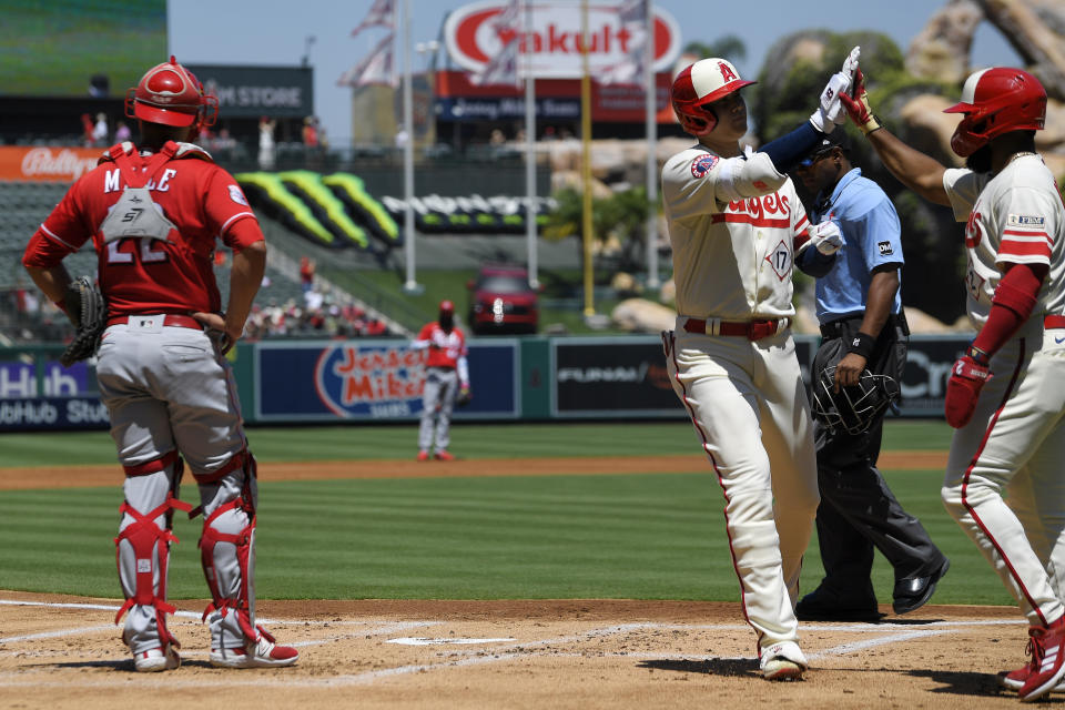 Los Angeles Angels' Shohei Ohtani, second from right, is congratulated by Luis Rengifo, right, after hitting a two-run home run as Cincinnati Reds catcher Luke Maile stands at the plate during the first inning of a baseball game Wednesday, Aug. 23, 2023, in Anaheim, Calif. (AP Photo/Mark J. Terrill)