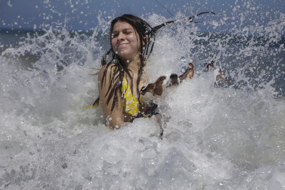 Mariana Rojas plays with her dog Sussy in the waves off Los Angeles beach after it recently reopened following a lockdown to contain the spread of COVID-19 in La Guaira, Venezuela, Friday, Oct. 23, 2020. Strict quarantine restrictions forced the closure of beaches across the country in March and reopened this week. (AP Photo/Matias Delacroix)