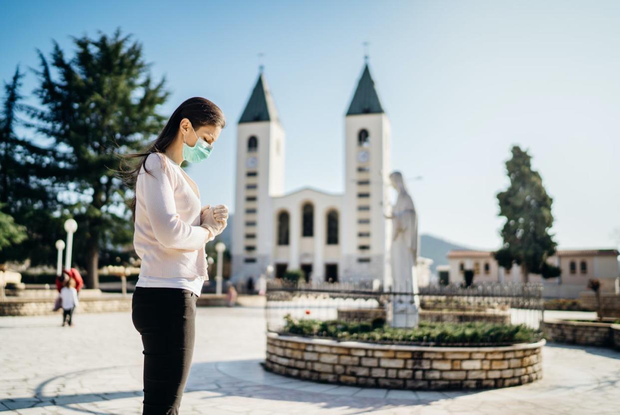 <span class="caption">COVID-19 is changing how people go on pilgrimages.</span> <span class="attribution"><a class="link " href="https://www.gettyimages.com/detail/photo/woman-wearing-mask-and-gloves-praying-to-god-due-to-royalty-free-image/1241966464?adppopup=true" rel="nofollow noopener" target="_blank" data-ylk="slk:conceptual,fashion,advertising/Moment via Getty Images;elm:context_link;itc:0;sec:content-canvas">conceptual,fashion,advertising/Moment via Getty Images</a></span>