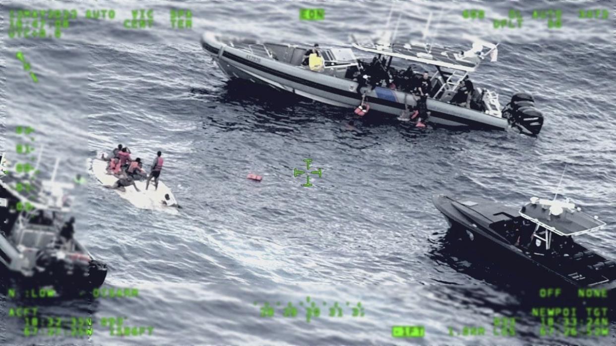 This photo released by the Seventh U.S. Coast Guard District shows people standing on a capsized boat, left, as some of its passengers are pulled up on to a rescue boat, top, in the open waters northwest of Puerto Rico, Thursday, May 12, 2022. 