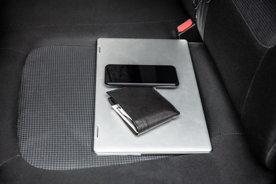 A black wallet, mobile phone, and laptop on the seat of a car.