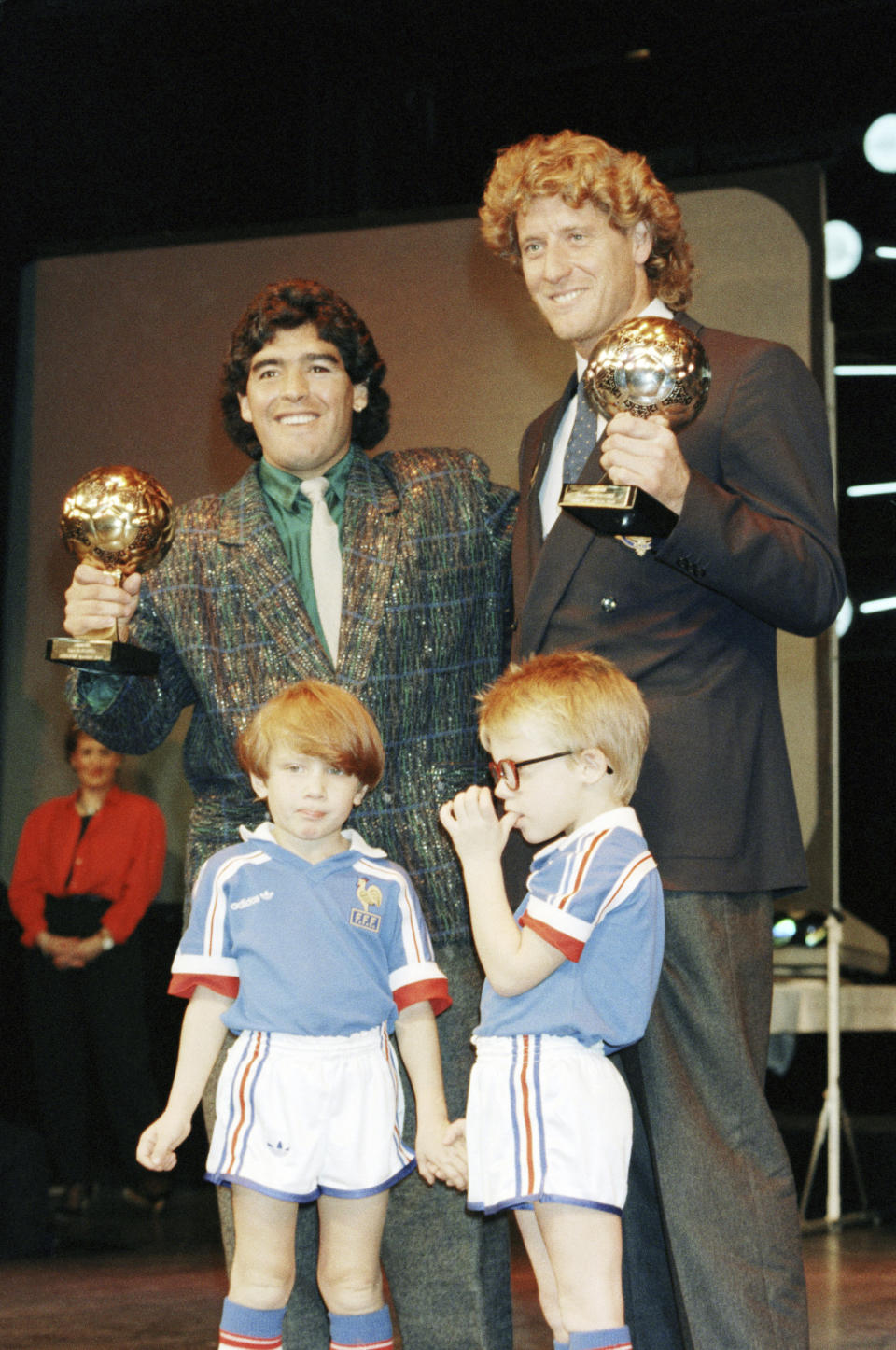 FILE - Argentina's soccer star Diego Maradona, left, and West German goalkeeper Harald Schumacher are holding their World Cup Soccer Ball awards while posing with two young soccer players during the Soccer Golden Shoe Award ceremony held in Paris, France, on Nov. 13, 1986. A trophy won by the late Diego Maradona for the best player at the 1986 World Cup that had mysterioulsy disappeared has resurfaced. It will be auctioned in Paris next month, the Aguttes house said on Tuesday May 7, 2024. (AP Photo/Michael Lipchitz, File)