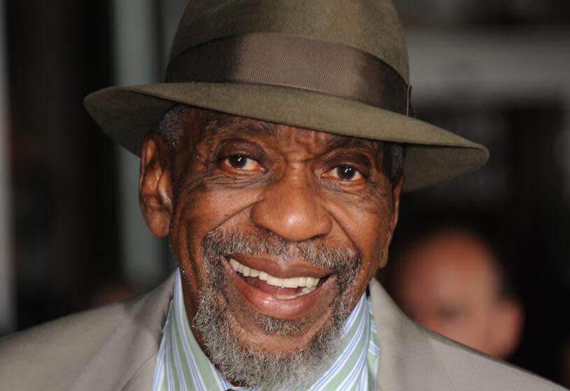 Bill Cobbs smiling broadly in a taupe suit and greenish-brown fedora