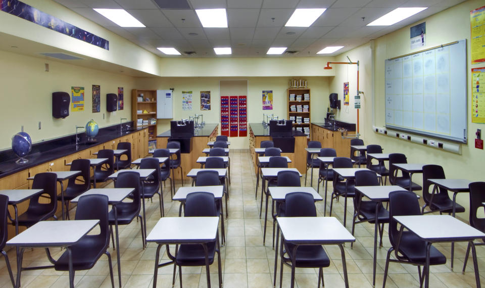 Classroom with rows of empty black chairs and desks, laboratory workstations at the back, educational posters on walls, and a large whiteboard