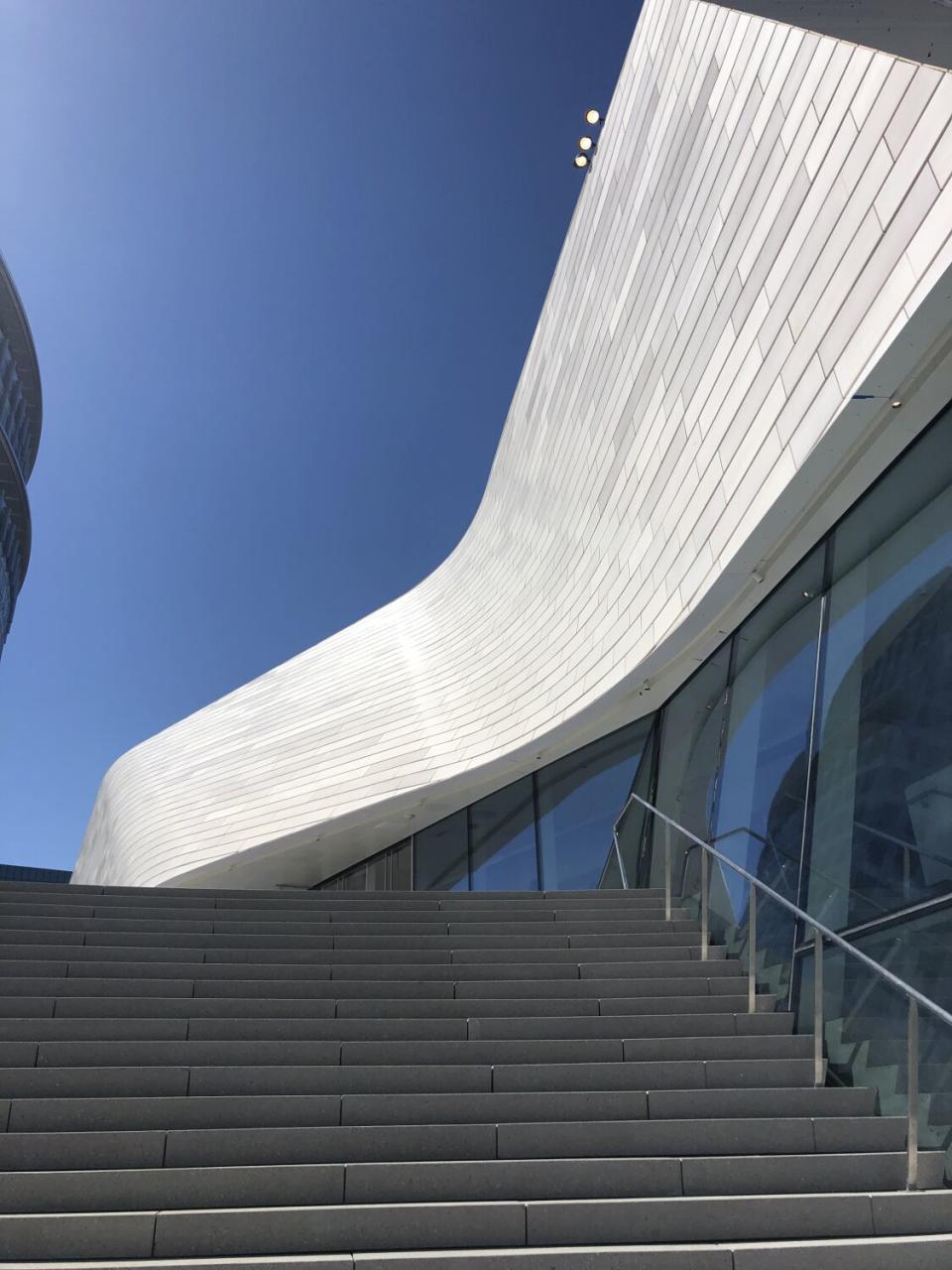 A view up a flight of concrete stairs reveals an undulating roof line covered in white terra-cotta tile