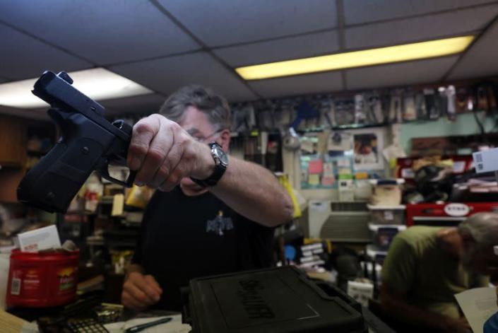 Rich Selmeyer, co-owner of The Gun Shop at MacGregor's, hands a firearm to a person for inspection in Lake Luzerne
