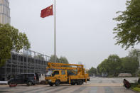 A worker eats his meal near preparations for a national memorial with a Chinese national flag flown at half staff in Wuhan in central China's Hubei province on Friday, April 3, 2020. Sidewalk vendors wearing face masks and gloves sold pork, tomatoes, carrots and other vegetables to shoppers Friday in the Chinese city where the coronavirus pandemic began as workers prepared for a national memorial this weekend for health workers and others who died in the outbreak. (AP Photo/Ng Han Guan)