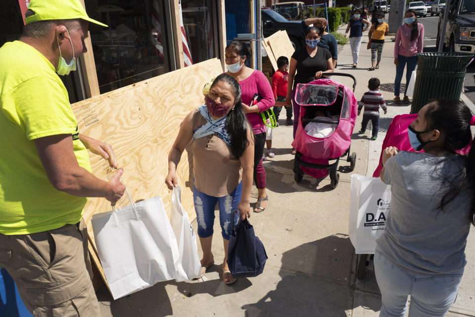 James Killoran, left, Executive Director of the Fuller Center for Housing, hands bags of food and diapers to people, Tuesday, June 9, 2020, during the coronavirus pandemic in New Rochelle, N.Y. (AP Photo/Mark Lennihan)