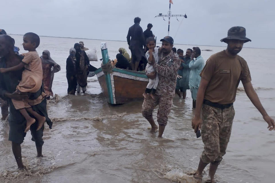 In this picture released by Pakistan's Sindh Rangers, paramilitary soldiers help to evacuate people from a village due to Cyclone Biparjoy approaching, at a costal area of Thatta district, in Pakistan's Sindh province, Tuesday, June 13, 2023. Pakistan's army and civil authorities are planning to evacuate 80,000 people to safety along the country's southern coast, and thousands in neighboring India sought shelter ahead of Cyclone Biparjoy, officials said. (Pakistan's Sindh Rangers via AP)