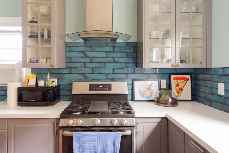 Light blue kitchen with grey cabinets, white countertop and stainless steel appliances.