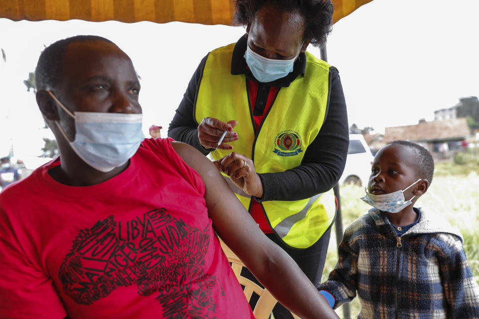A Kenyan man receives a dose of AstraZeneca coronavirus vaccine donated by Britain, as his son watches, at the Makongeni Estate in Nairobi, Kenya Saturday, Aug. 14, 2021. In late June, the international system for sharing coronavirus vaccines sent about 530,000 doses to Britain – more than double the amount sent that month to the entire continent of Africa. It was the latest example of how a system that was supposed to guarantee low and middle-income countries vaccines is failing, leaving them at the mercy of haphazard donations from rich countries.(AP Photo/Brian Inganga)