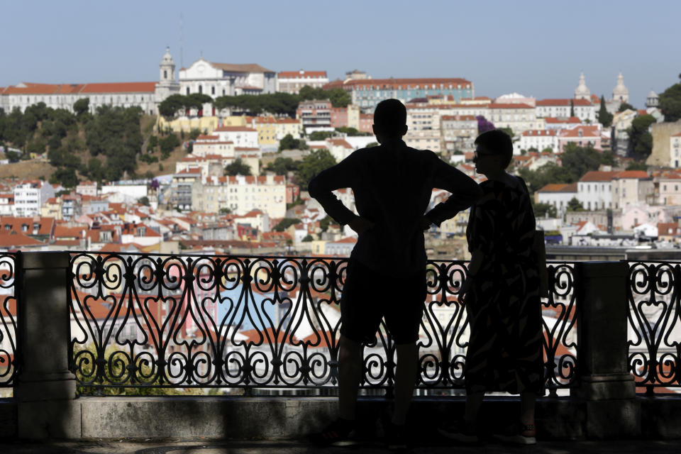 A couple look at Lisbon's skyline from a public garden, Thursday, July 1, 2021. Portugal's government says that from Friday it is imposing an 11 p.m. curfew in parts of the country that are seeing a surge in new COVID-19 cases including Lisbon. (AP Photo/Armando Franca)