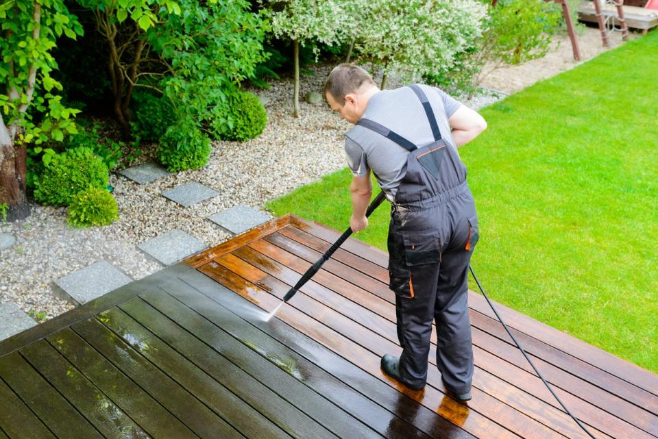Man wearing overalls cleaning a wooden deck with a power washer