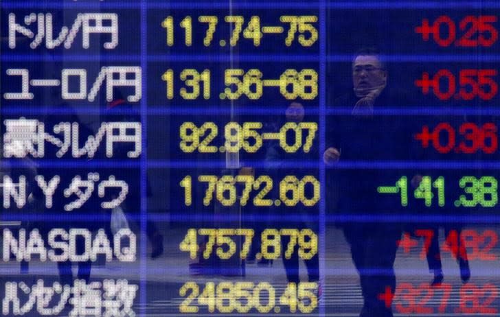 A pedestrian is reflected on an electronic board showing exchange rates between (from top row to third row) the Japanese yen against the U.S. dollar, the euro, and Australian dollar, and market indices of Dow Jones, NASDAQ, and the Hang Seng Index, outside a brokerage in Tokyo, January 26, 2015. REUTERS/Yuya Shino