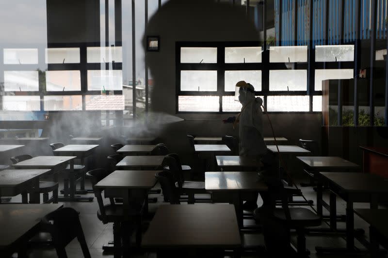 An Indonesian Red Cross personnel wearing a protective gear sprays disinfectant inside a classroom of a school, in Jakarta