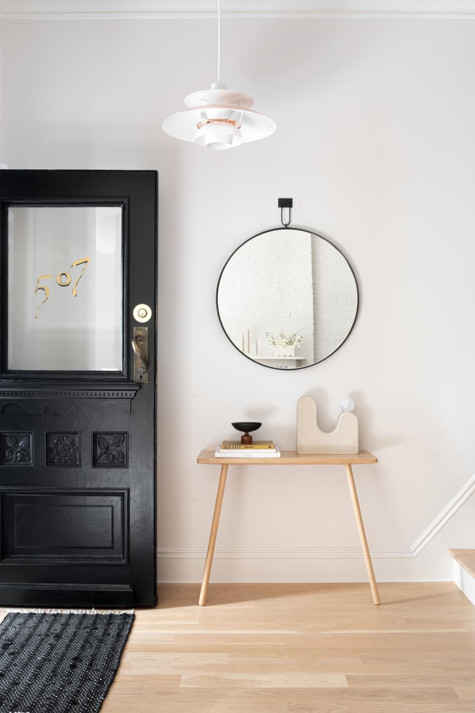 AFTER: The designers swapped wallpaper for white paint, and parquet flooring for neutral white oak planks. Simpler decor—and a freshly painted black door—add to the clean and modern look.