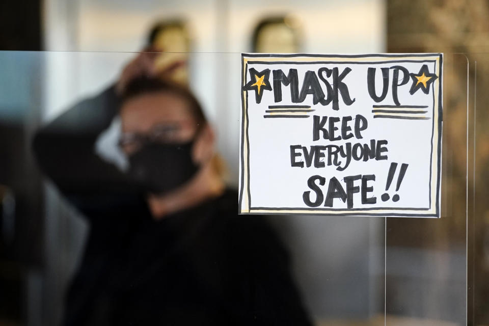 FILE - In this Tuesday, Nov. 17, 2020 file photo, manager Yllka Murati waits for a delivery driver to pick up takeout orders behind a partition displaying a sign to remind customers to wear a mask, at the Penrose Diner, in south Philadelphia. Despite the expected arrival of COVID-19 vaccines in just a few weeks, it could take several months — probably well into 2021 — before things get back to something close to normal in the U.S. and Americans can once again go to the movies, cheer at an NBA game or give Grandma a hug. (AP Photo/Matt Slocum, File)