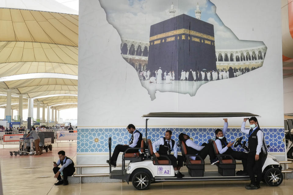 Golf cart drivers wait for the arriving pilgrims under a billboard showing the Kaaba, the cubic building at the Grand Mosque, at the Hajj terminal of King Abdulaziz International Airport in Jeddah, Saudi Arabia, Tuesday, June 20, 2023. Saudi Arabia has ambitious plans to welcome millions more pilgrims to Islam's holiest sites. But as climate change heats an already scorching region, the annual Hajj pilgrimage could prove even more daunting. (AP Photo/Amr Nabil)