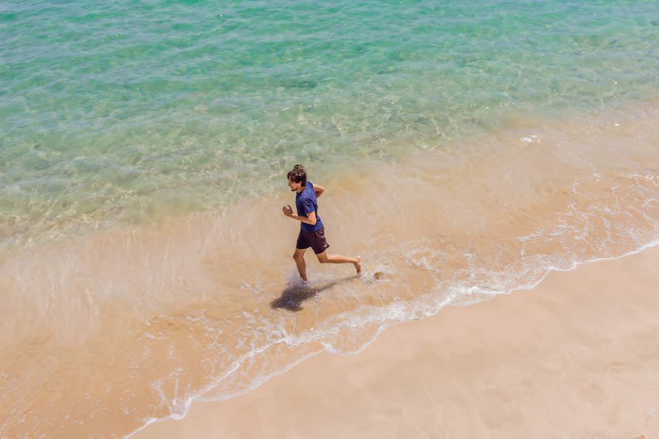 Runner running on beach by the ocean - view from above.