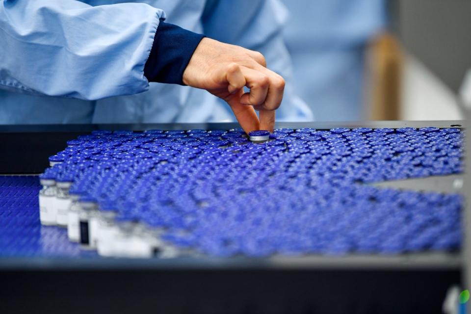 Person picking up a glass vial among many on a conveyor belt.