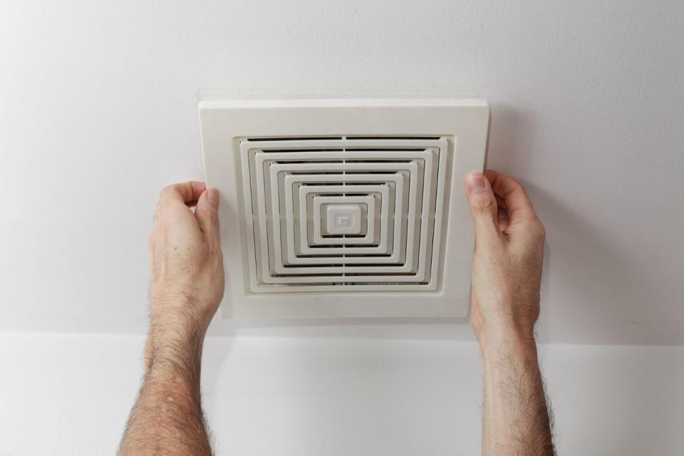 A person with only their hands visible installs a bathroom exhaust fan on a ceiling.