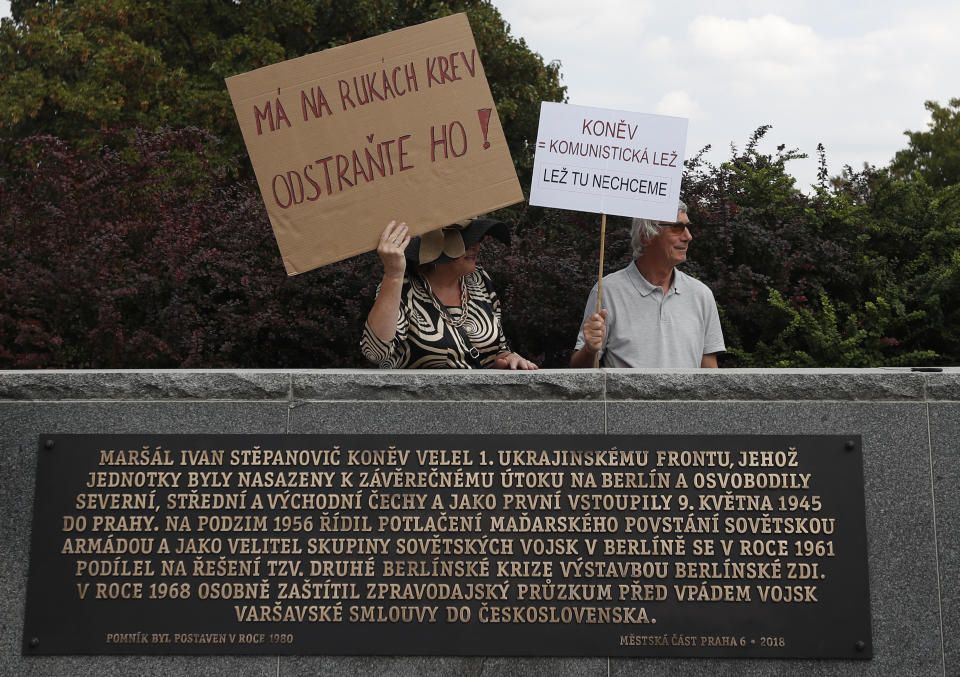Residents stand behind a newly unveiled explanatory text about the role of Soviet World War II commander Ivan Stepanovic Konev at Konev's monument in Prague, Czech Republic, Tuesday, Aug. 21, 2018. The new text describes Konev's leading role in crushing the 1956 anti-Soviet uprising in Hungary, his contribution to the construction of the Berlin Wall and the preparation of the 1968 invasion of Czechoslovakia. On Tuesday, Czech Republic is marking the 50th anniversary of the 1968 Soviet-led invasion of Czechoslovakia. Text on left banner reads: "He has blood on his hands. Remove him!". Text on right banner reads: "Kolev-Communist lie. We don't want the lie here". (AP Photo/Petr David Josek)