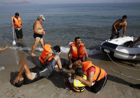 A tourist walks past an Iranian migrant collapsing next to his son and crying wife moments after a small group of exhausted migrants from Iran arrived by paddling an engineless dinghy from the Turkish coast (seen in the background) at a beach on the Greek island of Kos August 15, 2015. REUTERS/Yannis Behrakis