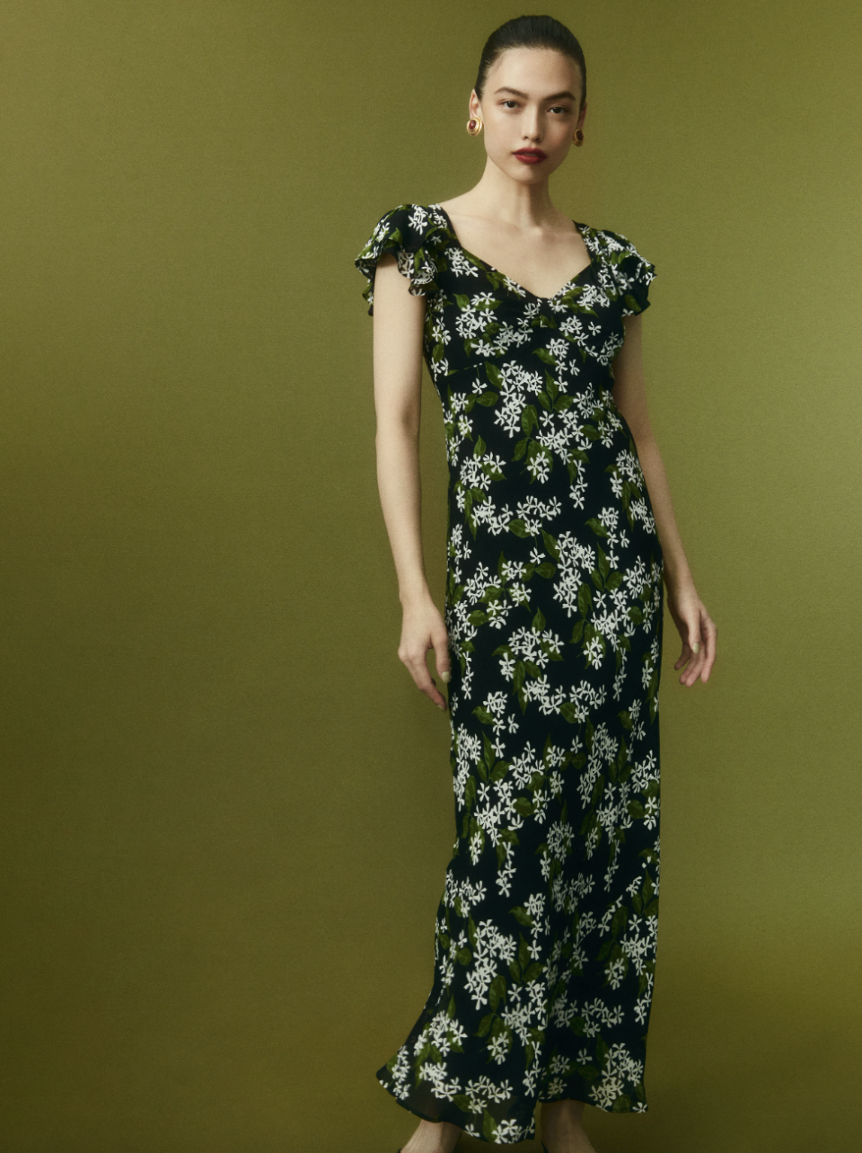 model wearing black dress with white and green floral print, Lisola Dress (Photo via Reformation)