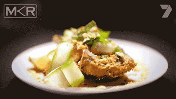 A plate of gourmet food with sliced vegetables and a garnish. The entree caption says: "Sudanese Lamb Cutlets With Peanut Sauce And Cucumber Salad"