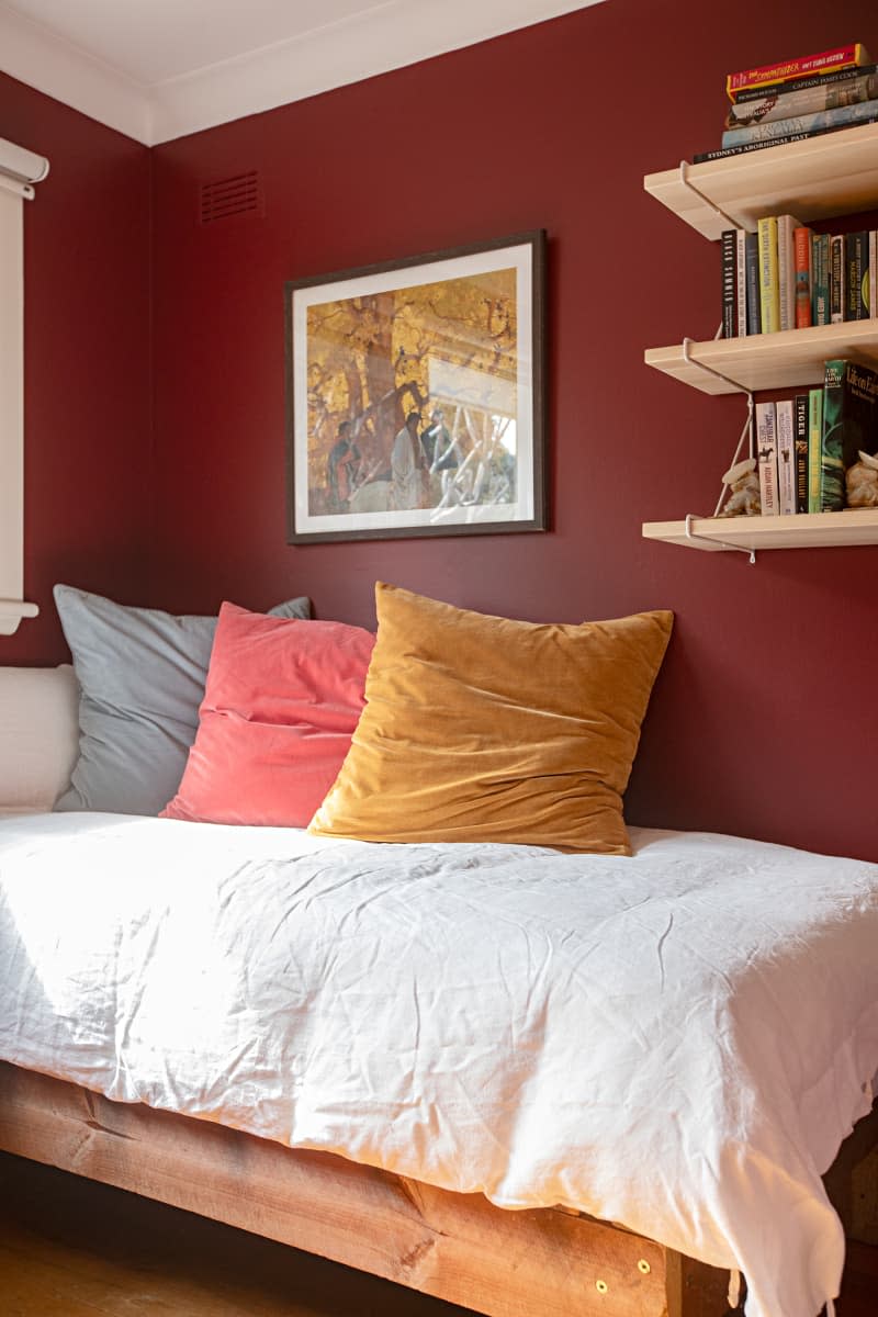 small bed in maroon room with wood bookshelves