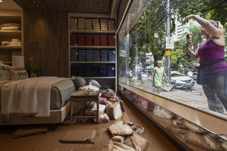 A woman takes a photo of a muddied store after heavy rains triggered flooding in Belo Horizonte, Minas Gerais state, Brazil, Wednesday, Jan. 29, 2020. The deadly rains are expected to continue on Wednesday in Minas Gerais, where some municipalities have declared a state of emergency. (AP Photo/Gustavo Andrade)