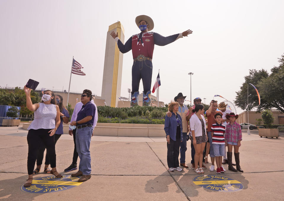 With the famous giant Big Tex as the background, families pose for photos during a drive-thru visit to Fair Park in Dallas, Saturday, Sept. 19, 2020. Although the State Fair of Texas was canceled this year due to COVID-19, fair organizers are holding drive-thru visits starting this weekend. (AP Photo/LM Otero)