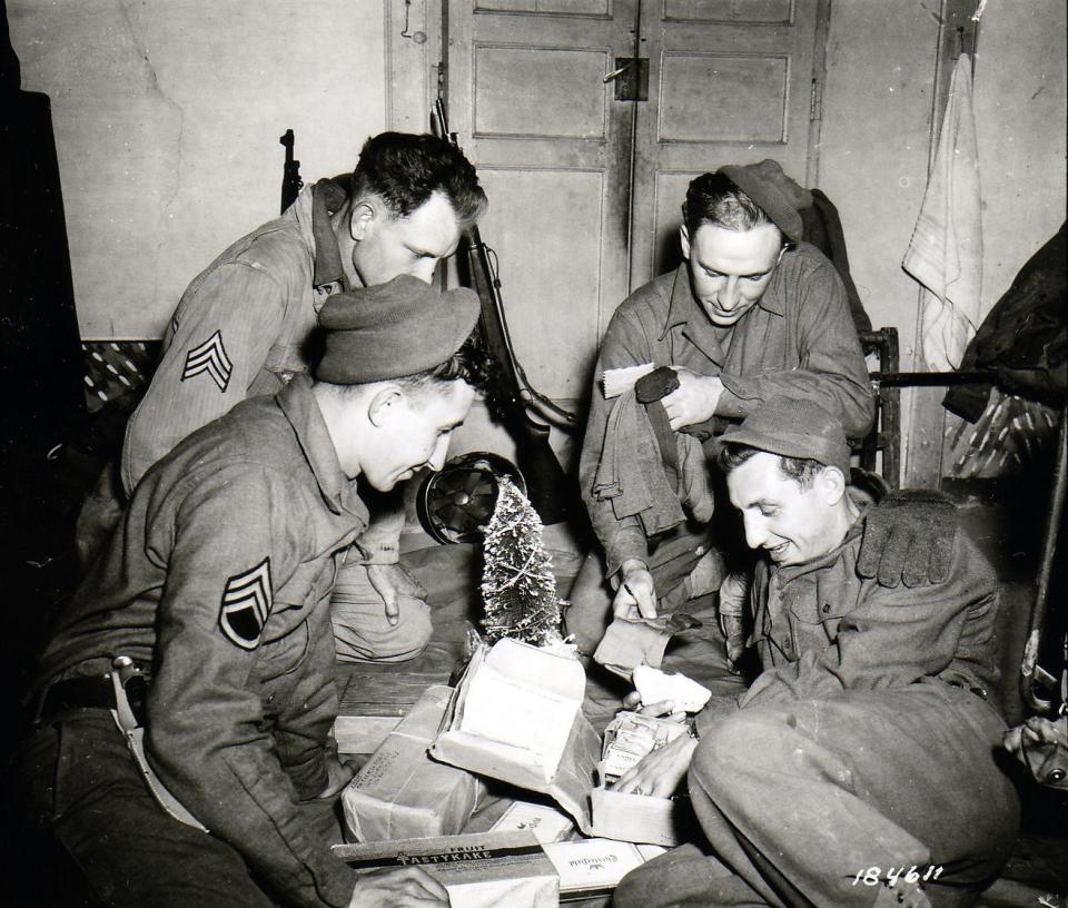 US Soldiers sitting around a miniature Christmas tree and opening a Christmas package in Pietramelara, Italy. December 16, 1943.