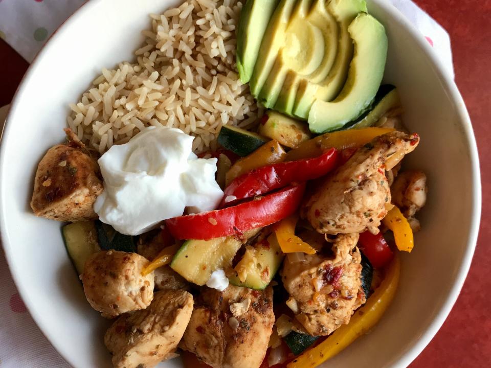 A bowl of rice, chicken, peppers, avocado, and Greek yogurt.