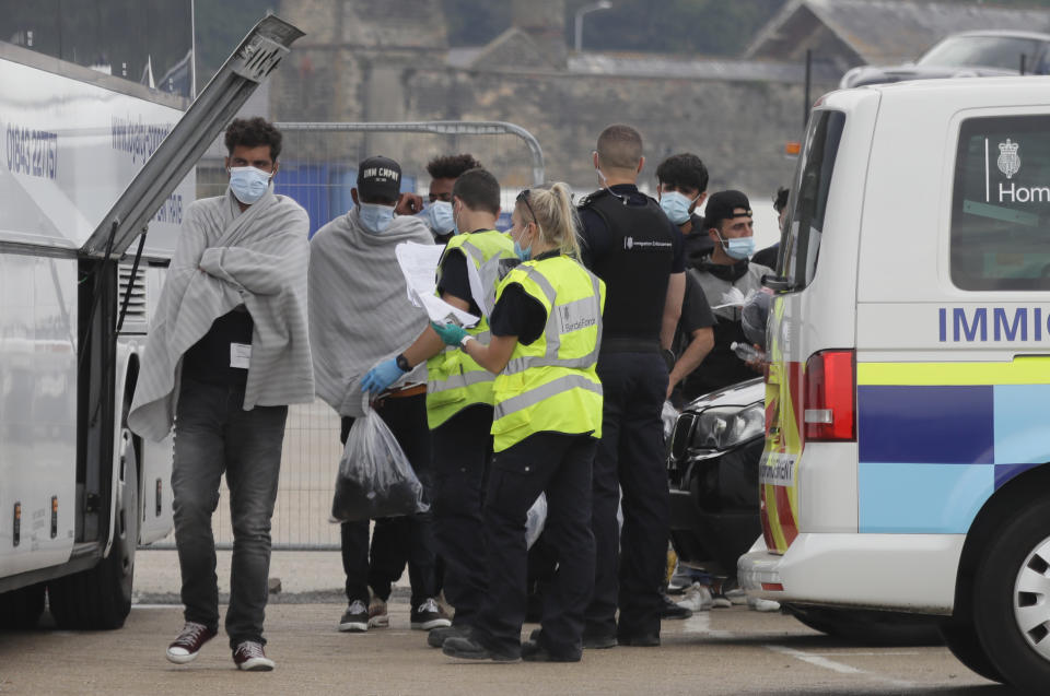 Border Force officers escort a group of men thought to be migrants to a waiting bus in the port city of Dover, England, Saturday Aug. 8, 2020. The British government says it will strengthen border measures as calm summer weather has prompted a record number of people to attempt the risky sea crossing in small vessels, from northern France to England. (AP Photo/Kirsty Wigglesworth)