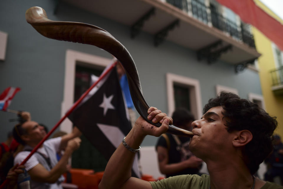 A young man blows on a ram's horn during protest outside the executive mansion known as La Fortaleza, in Old San Juan, demanding the resignation of Governor Wanda Vazquez after the discovery of an old warehouse filled with unused emergency supplies, in San Juan, Puerto Rico, Monday, Jan. 20, 2020. Anger erupted on Saturday after an online blogger posted a live video of the warehouse in the southern coastal city of Ponce filled with water bottles, cots, baby food and other basic supplies that had apparently been sitting there since Hurricane Maria battered the U.S. territory in September 2017. (AP Photo/Carlos Giusti)