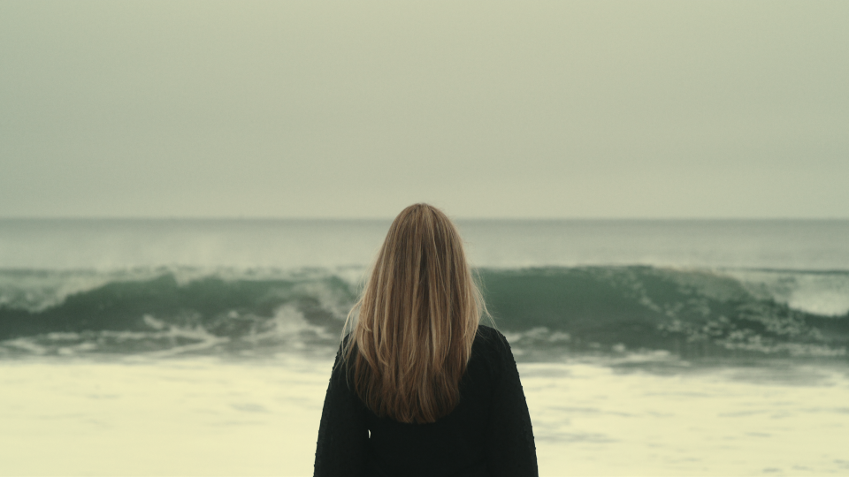 A woman with her back to camera, facing the beach; still from "American Nightmare"