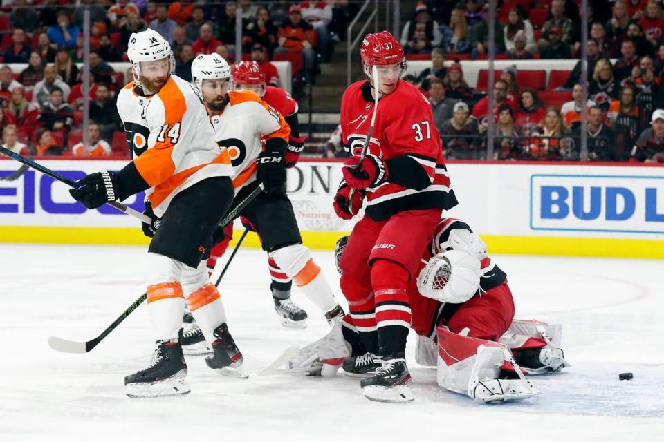 Philadelphia Flyers center Sean Couturier (14) and Carolina Hurricanes right wing Andrei Svechnikov (37), of Russia, keep an eye on the puck, behind Hurricanes goaltender James Reimer during the first period of an NHL hockey game in Raleigh, N.C., Tuesday, Jan. 7, 2020. (AP Photo/Gerry Broome)